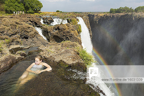 Young teenage girl in the water at the Devils Pool  on the cliff top overlooking Victoria Falls  Zambia  view from above.