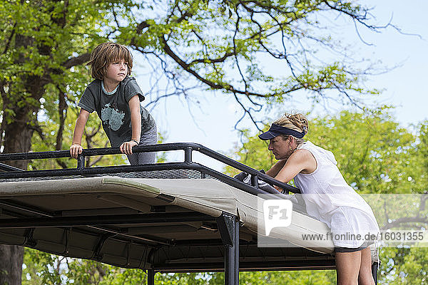 Ein fünfjähriger Junge und ein Teenager-Mädchen auf der Beobachtungsplattform eines Safarijeeps unter Bäumen.