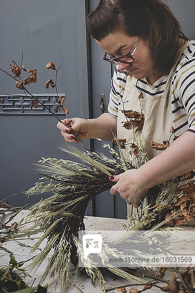 Frau macht einen Winterkranz  fügt getrocknete Gräser und Samenköpfe und Zweige mit braunen Blättern hinzu.