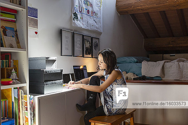 Girl sitting in her bedroom  doing homework during Coronavirus lockdown.