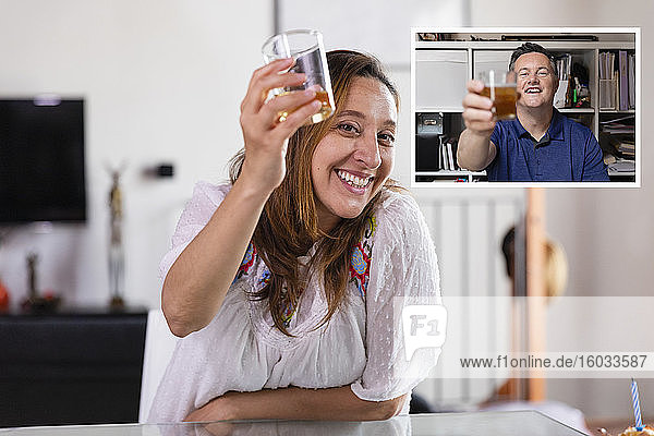 Mann und Frau halten ein Getränk in der Hand und stoßen während der Coronavirus-Sperre online an  während sie sich unterhalten.