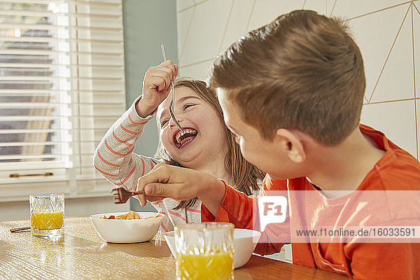 Junge und Mädchen sitzen am Küchentisch und essen Frühstück.