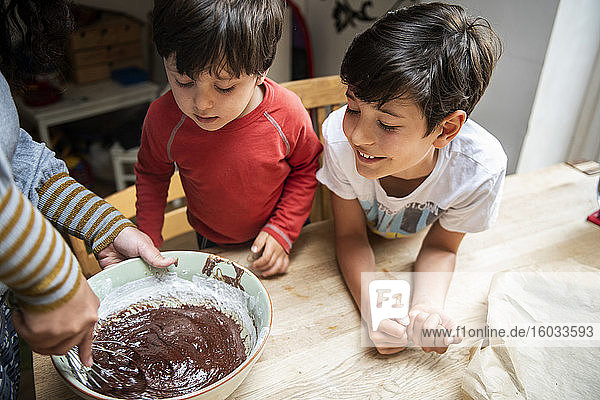 Zwei Jungen mit schwarzen Haaren sitzen an einem Küchentisch und backen Schokoladenkuchen.