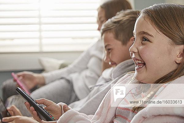 Group of children sitting on a sofa in their pajamas  watching television.