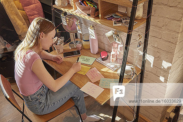 Teenagerin  die in ihrem Zimmer an einem Schreibtisch sitzt und motivierende Zitate auf Zettelkarten schreibt.