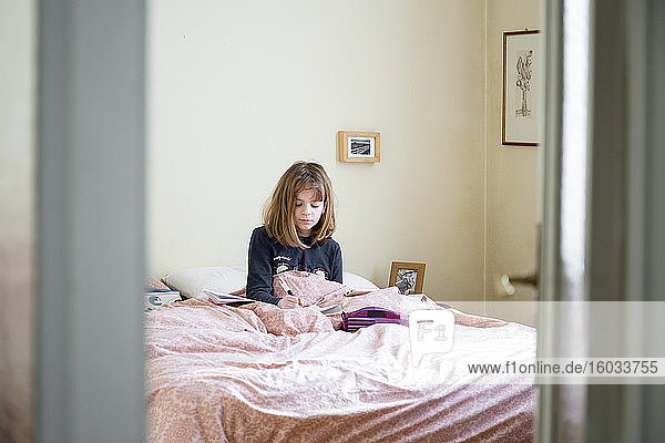 Mädchen sitzt auf ihrem Bett in ihrem Zimmer  lernt  Hausunterricht mit Laptop und Notebook