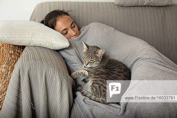 Frau und grau gestromte Katze schlafen auf einem Sofa.