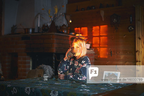 Mädchen sitzt an einem Tisch in einer Blockhütte  trinkt ein Glas Wasser  Vasterbottens Lan  Schweden.