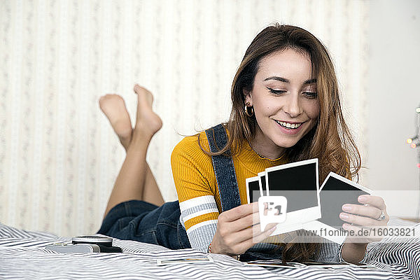 Junge Frau mit langen braunen Haaren liegt auf dem Bett und betrachtet Polaroidfotos.
