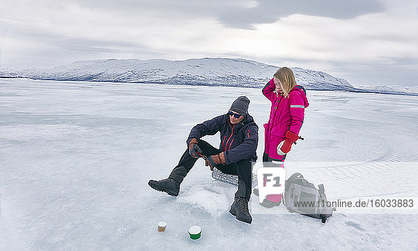 Mädchen und Mann beim Eisfischen auf dem zugefrorenen See in Vasterbottens Lan  Schweden.