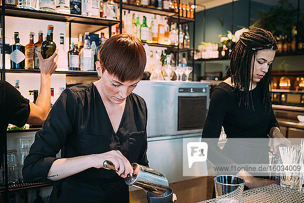 Zwei schwarz gekleidete junge Frauen stehen hinter der Theke und bereiten Getränke vor.