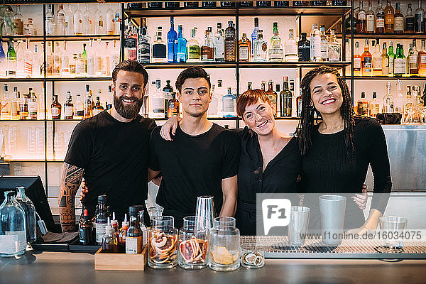 Porträt von zwei jungen Frauen und Männern in schwarzer Kleidung  die in einer Bar arbeiten und in die Kamera lächeln.
