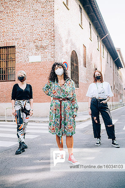 Drei junge Frauen  die während des Corona-Virus Gesichtsmasken trugen und auf einem Fußgängerüberweg in einer Straße standen.
