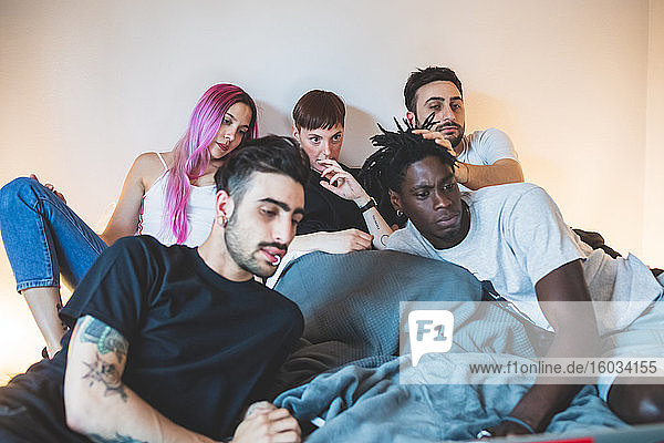 Group of young men and women lying on a bed  looking at laptop.