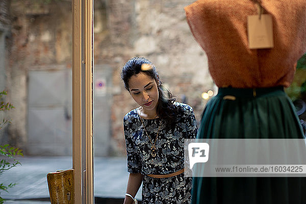 Woman with long black hair looking at skirt on mannequin in shop window.