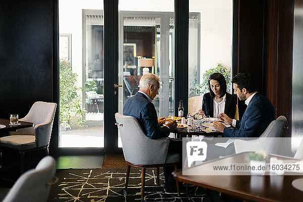 Two businessmen and woman having working lunch in hotel restaurant