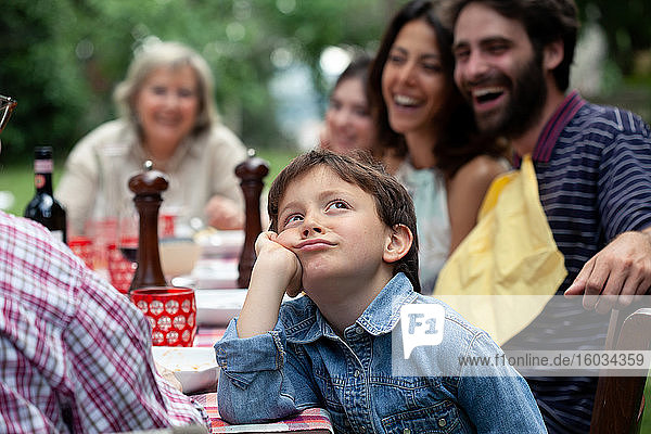 Gelangweilter Junge beim Familienessen im Freien