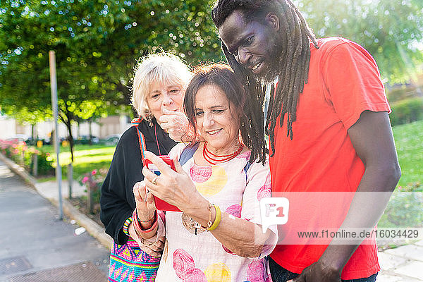 Schwarzer Mann mit Dreadlocks und zwei kaukasische Frauen stehen auf der Brücke und schauen auf ein Mobiltelefon.