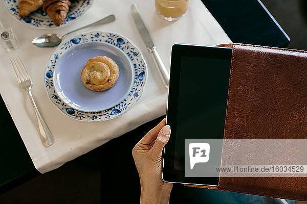 Frauenhand entfernt digitales Tablett aus dem Koffer beim Frühstück im Boutique-Hotel in Italien