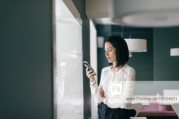 Junge Geschäftsfrau im Hotel schaut auf Smartphone