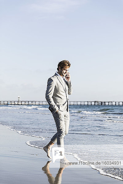 Barfüssiger Geschäftsmann spricht mit einem Smartphone am sonnigen Strand des Ozeans  Los Angeles  Kalifornien