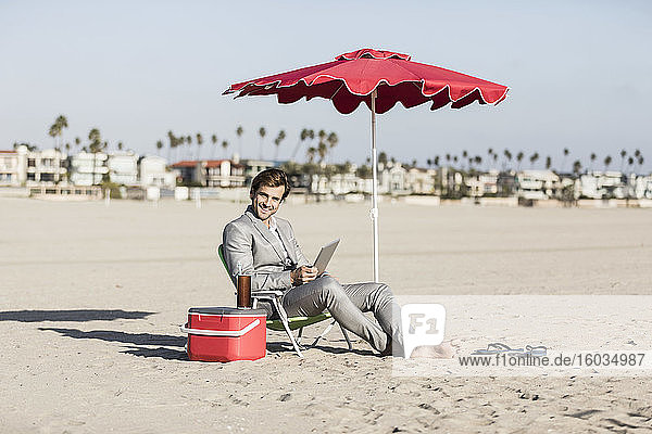 Porträt eines glücklichen barfüssigen Geschäftsmannes  der am sonnigen Strand arbeitet  Los Angeles  Kalifornien