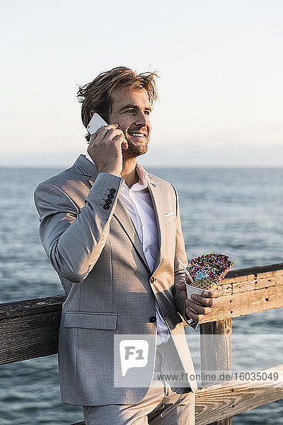 Geschäftsmann mit Eistüte spricht am Smartphone am Ozeanpier
