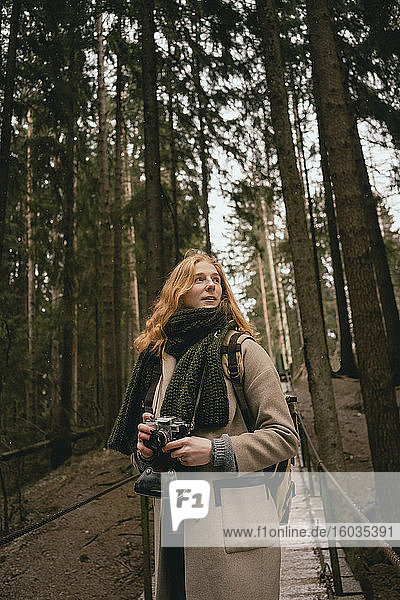 Rothaarige Frau mit Kamera auf Waldsteg