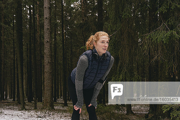 Weibliche Läuferin ruht mit den Händen auf den Knien in verschneiten Wäldern