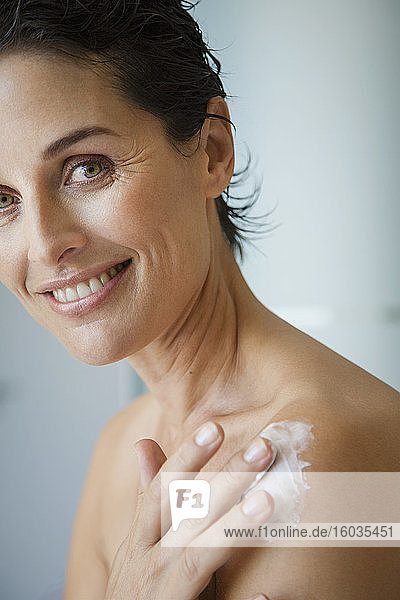 Porträt einer glücklichen Frau  die Feuchtigkeitscreme auf die Schulter aufträgt