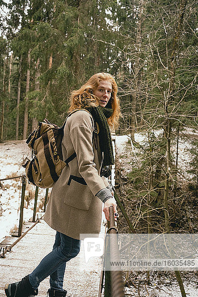 Portrait redhead woman with backpack on footbridge in snowy woods