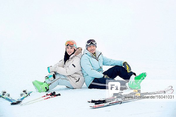 Glückliche junge Paare sitzen Rücken an Rücken im Schnee