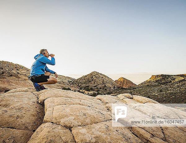 USA  Utah  St. George  Man crouching in rocky landscape and drinking water after running