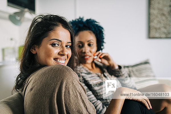 Smiling young woman with friend sitting on sofa at home