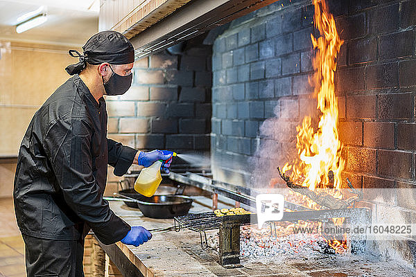 Traditional cooking of paella in restaurant kitchen  chef wearing protective mask