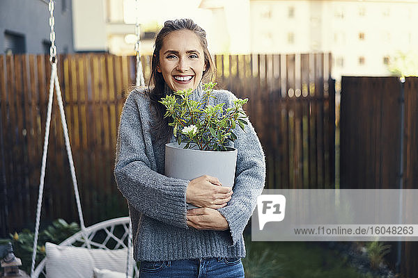 Fröhliche junge Frau  die eine Topfpflanze trägt  während sie im Garten steht
