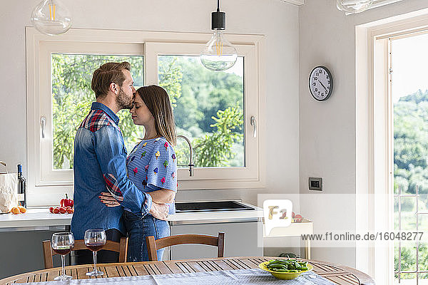 Mann küsst Frau  während er in der Küche zu Hause am Esstisch steht