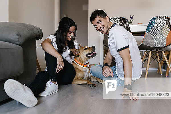 Smiling couple sitting with dog on floor at home