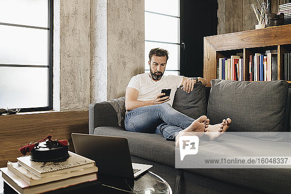 Mature man sitting on couch  using smartphone