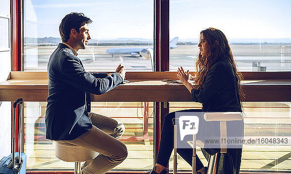 Business couple talking while sitting at airport cafe