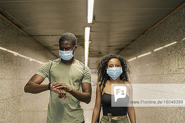 Pärchen mit Masken im unterirdischen Gang einer U-Bahn-Station