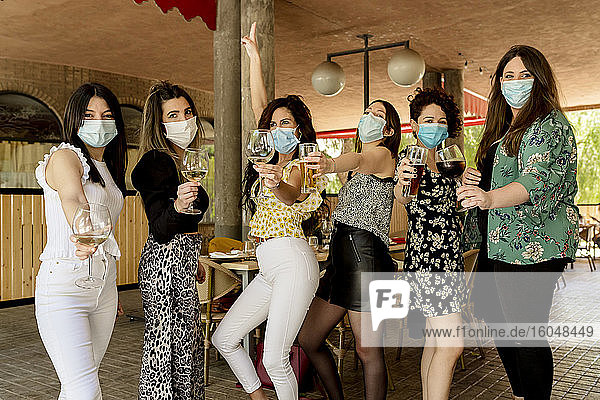 Young female customers holding drinks while standing at restaurant during pandemic