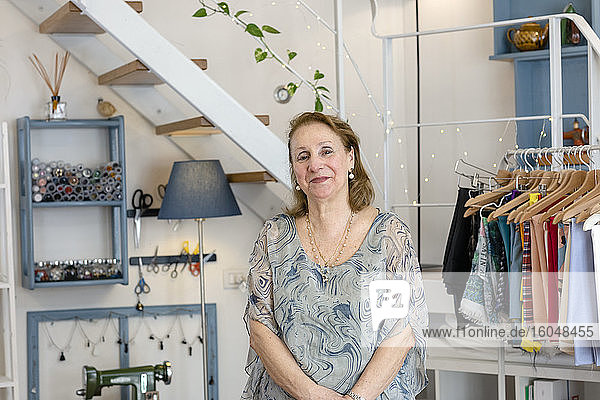 Smiling senior female design professional standing at illuminated fashion studio