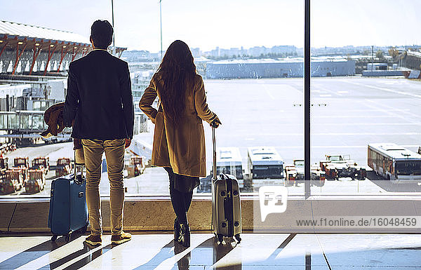 Business couple looking through window at airport departure area