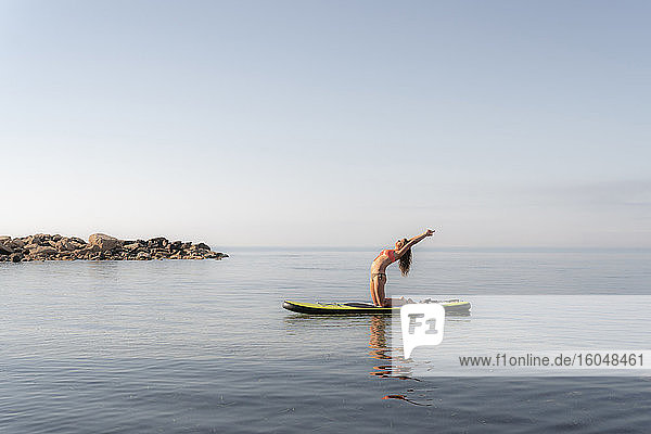 Ältere Frau übt Yoga auf Paddleboard auf dem Meer gegen den Himmel