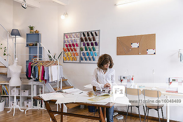 Weibliche Modeunternehmerin sieht sich eine Zeitschrift an  während sie an einer Werkbank im Designstudio steht
