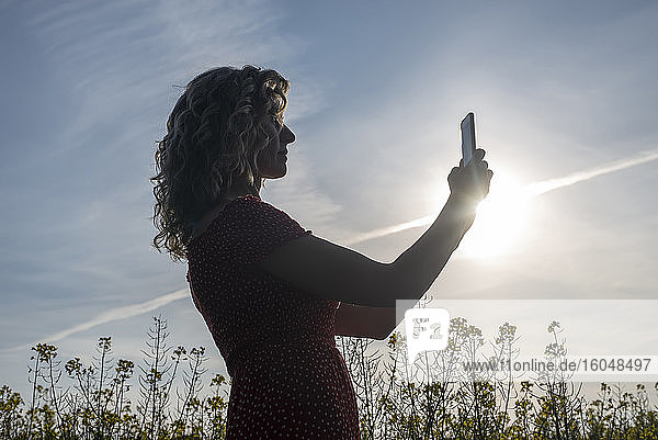 Silhouette reife Frau  die ein Smartphone benutzt  während sie gegen den Himmel bei Sonnenuntergang steht
