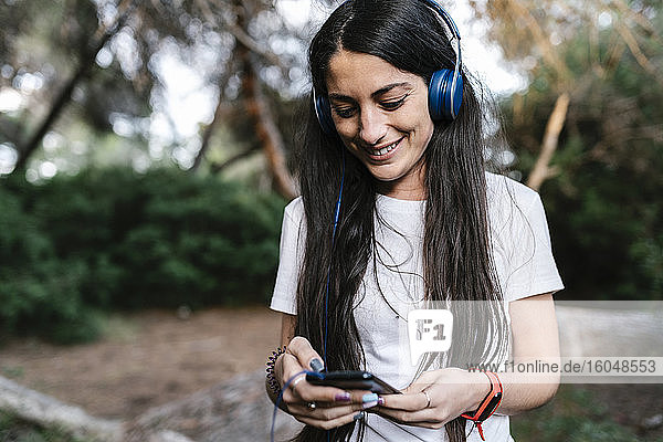 Woman with headset using smartphone in the woods