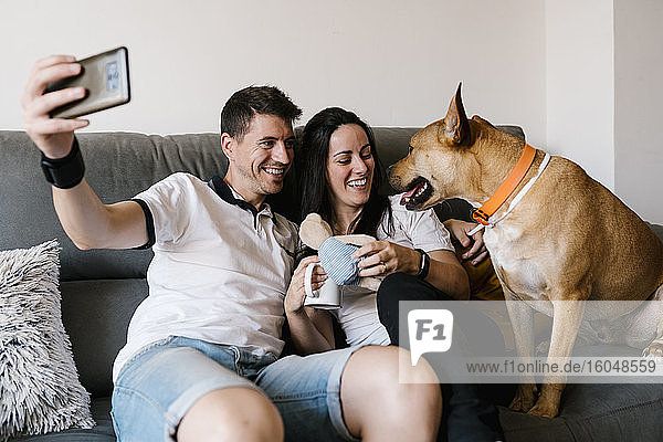Lächelndes Paar macht Selfie mit Hund zu Hause