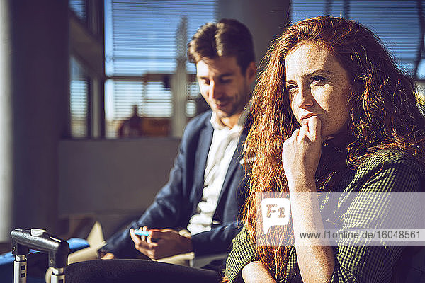 Nachdenkliche Geschäftsfrau sitzt mit Mann im Abflugbereich des Flughafens